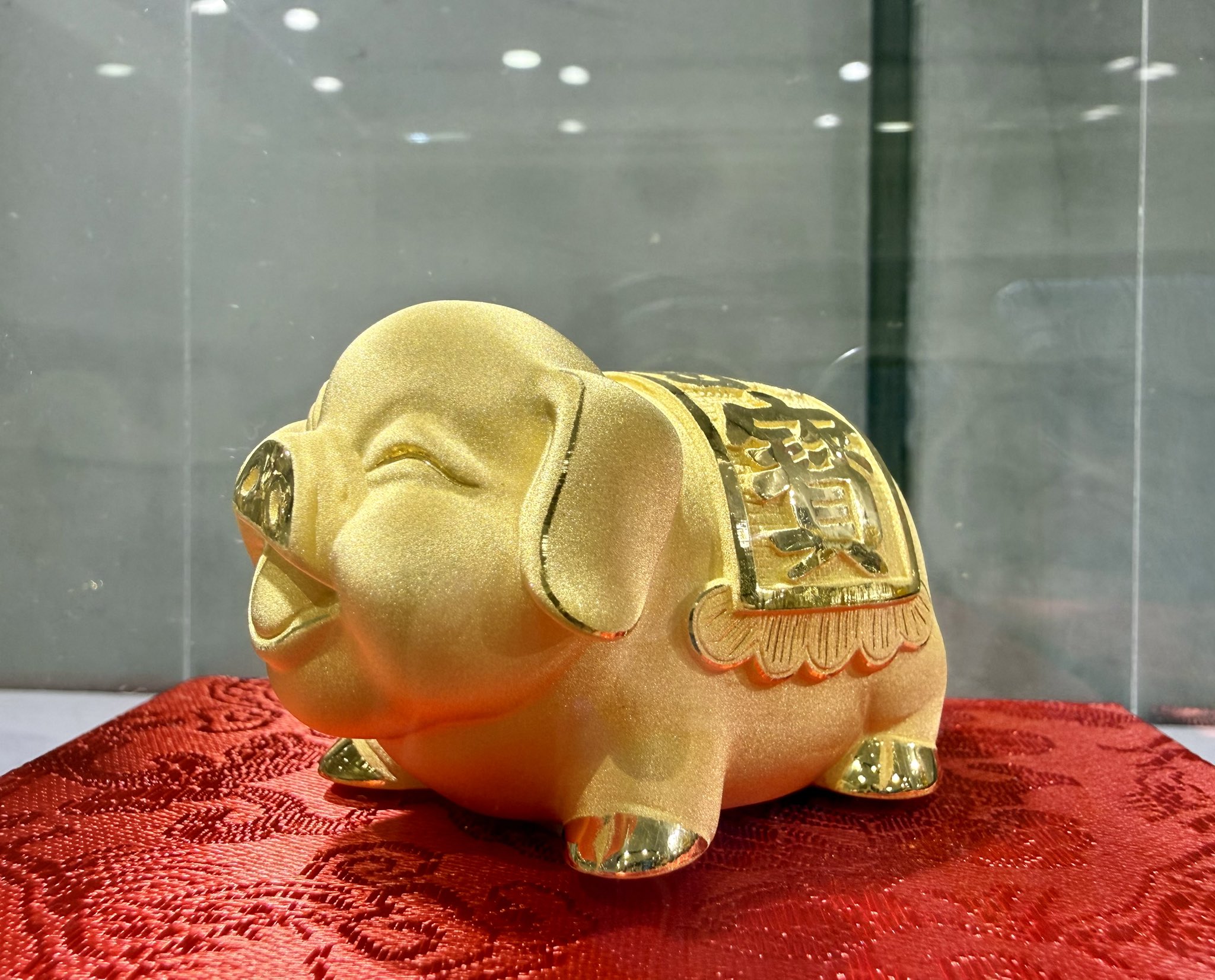 Petit cochon en or massif 24 carats frappé du caractère 福 (bonheur), posé sur de la soie rouge brodée